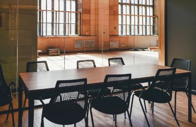 A meeting room with a long table and a row of chairs beside tall windows.